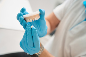A dentist showing how a dental crown fits onto a plaster tooth model