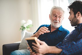 A senior man speaking to a younger man while sitting on a couch