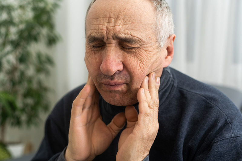 Older patient rubbing their gums due to ill-fitting dentures